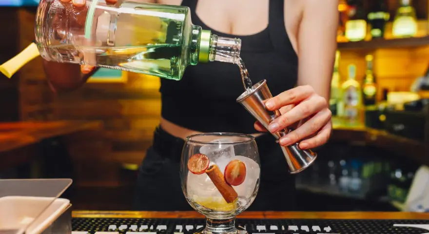 Barman nalewa alkohol z butelki do miarki nad kieliszkiem z lodem i owocami.